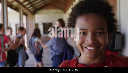 Smiling boy in red top wearing backpack straps standing in school corridor, with brick wall Stock Photo