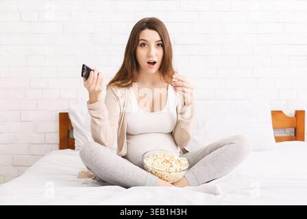 Expecting Mother Enjoys Relaxed Time Watching Screen While Snacking on Popcorn in Cozy Setting Stock Photo