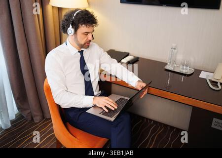 Professional man typing on laptop in hotel room workspace during trip Stock Photo