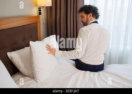 Businessman Arranging Pillow on Hotel Bed After Work Trip Stock Photo