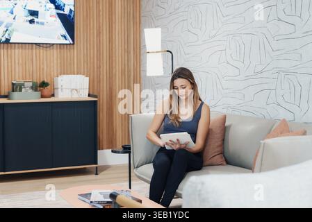 Female Engaged With Tablet On Sofa. Woman Deeply Involved In Electronic Notetaking At Home. Lady Absorbed In Educational Activities Using Her Tablet Stock Photo