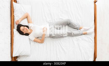 Woman in Gray Pajamas Resting Comfortably on a Bed in a Serene Indoor Setting Stock Photo