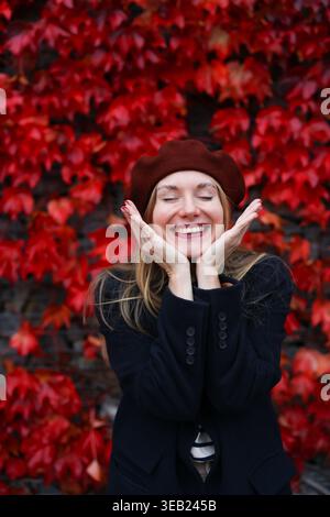 Happy woman in beret smiling against red autumn leaves, joyful lifestyle portrait. Stock Photo