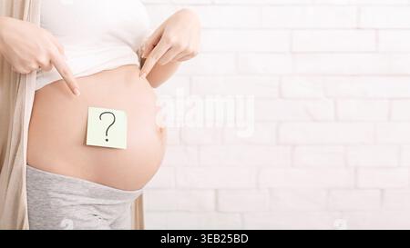 Expectant Mother Showcasing Baby Bump With Question Mark on Sticky Note Stock Photo