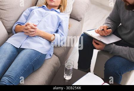 Depressed woman lying on sofa, consulting with psychologist at session Stock Photo