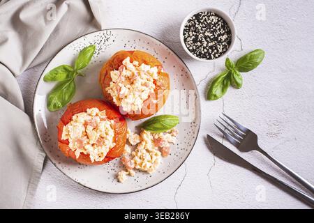 Baked tomato halves filled with scrambled egg and basil on a plate on the table top view Stock Photo