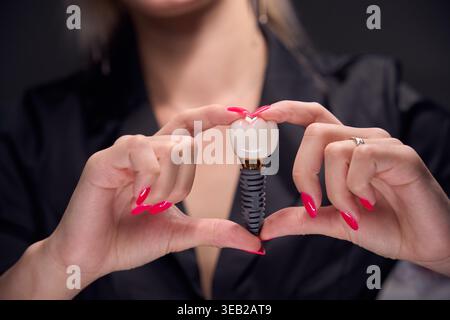 Adult woman presenting dental implant with crown in studio Stock Photo