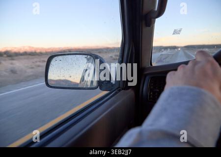 Driver's hands on steering wheel during desert road trip Stock Photo