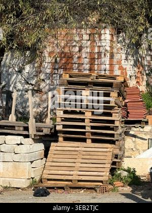 Stack of wooden pallets and bricks near textured wall outdoors, suitable for industrial background. Mobile photo Stock Photo