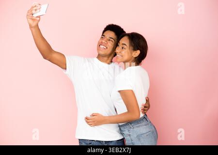 Young Couple Enjoys a Joyful Moment Taking Selfies Together in Front of a Pink Background Stock Photo