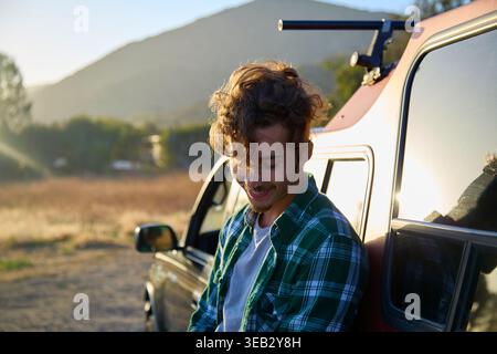 Young man laughing leaning on pickup truck in nature Stock Photo