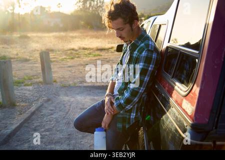 Young man contemplating outdoors leaning on truck during golden hour Stock Photo