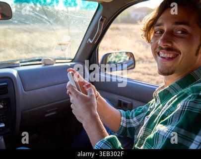Smiling man using phone while driving car Stock Photo