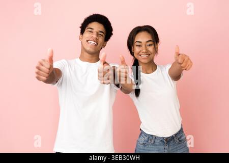 Pair of Young Individuals Smiling and Giving Thumbs up in Front of a Pink Background Stock Photo