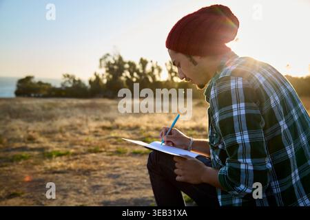 Man drawing in journal outdoors at sunset Stock Photo