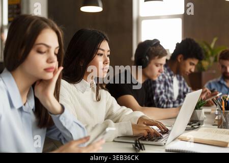 Diverse students sitting at college library, doing homework Stock Photo