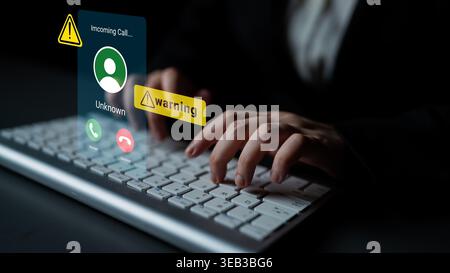 A person typing on a keyboard receives an incoming call alert displayed on a computer screen, featuring a warning symbol for an unknown caller. Gantry Stock Photo