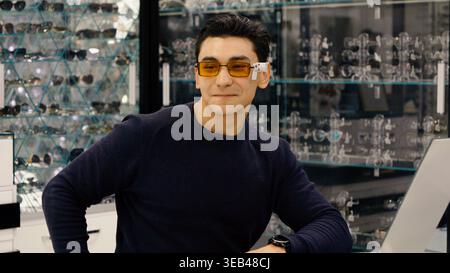 Stylish man wearing yellow sunglasses in optician shop Stock Photo