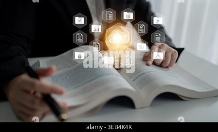 A person studies an open book while a glowing light bulb and cloud symbols represent innovation. This image showcases knowledge and technology Stock Photo
