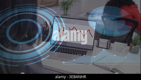 Displaying laptop showing red chart with blue HUD overlays at office desk, woman in red-orange top Stock Photo