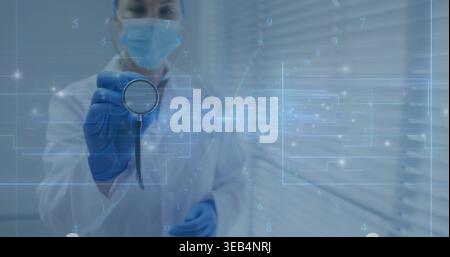 Holding stethoscope, masked woman MD in lab coat, blue gloves extending at camera in clinic overlay Stock Photo