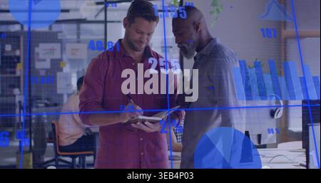 Two men in casual shirts standing reviewing notes in office holding notebook with blue charts Stock Photo