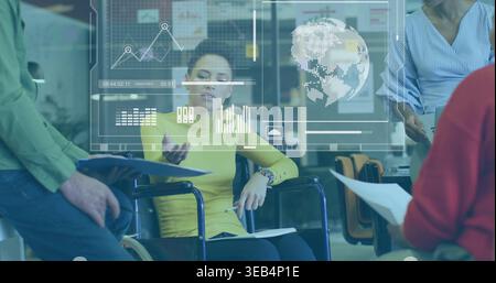 Leading woman in wheelchair wearing yellow gesturing with papers, pen and data charts in office Stock Photo