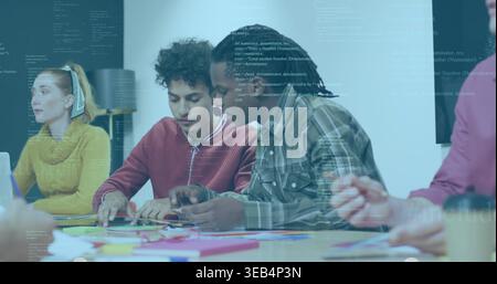 Collaborating group of four adults leaning over table in classroom, with colorful papers and laptop Stock Photo