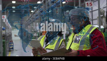 Inspecting inventory in warehouse, two staff in hi-vis gear using tablet, clipboard with AR map Stock Photo