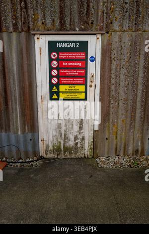 April 2026 - Aged doorway with warning signs into Hanger 2 at Goodwood Race circuit, West Sussex, England, UK. Stock Photo