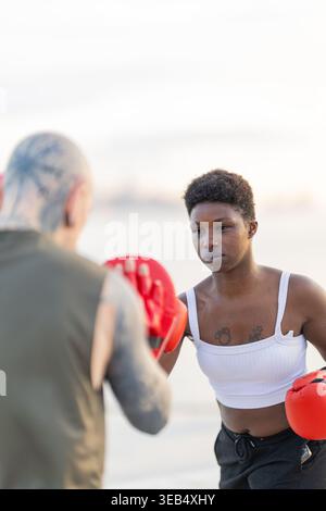 Black woman exercising in boxing gloves, practicing punches with a coach Stock Photo