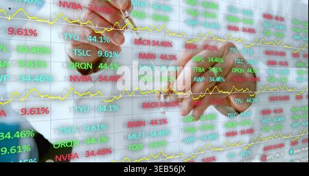 Examining trader pointing stylus at glass screen showing stocks, % values, yellow lines, white-cuff Stock Photo