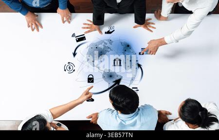 A diverse business team collaborates over a table, analyzing a digital world map with financial icons, symbolizing strategy, growth, and global Stock Photo