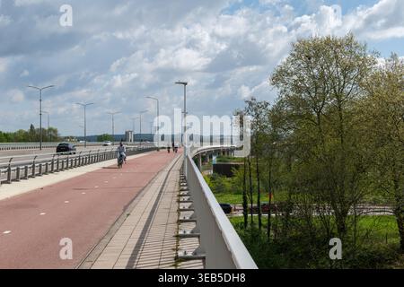 Dedicated cycle and pedestrian bridge spanning across landscape in Maastricht, Netherlands, with dramatic cloudy sky and geometric perspective lines. Stock Photo