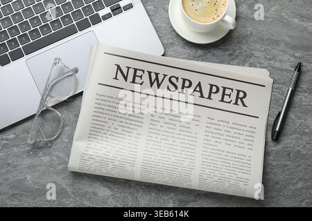 Newspaper, laptop, coffee, glasses and pen on grey desk, flat lay Stock Photo