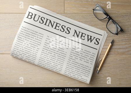 Newspaper, glasses and pen on wooden table, flat lay Stock Photo