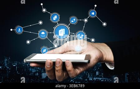 A hand holding a smartphone displays various network icons symbolizing digital interaction and communication in a modern urban landscape at night Stock Photo