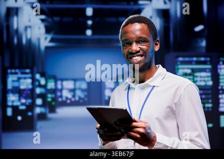 Portrait of smiling technician in front of supercomputers in high performance computing server room, ensuring flawless operations conditions. Expert monitoring data center hardware energy consumption Stock Photo