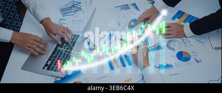 A business team is analyzing financial reports and charts on a laptop, showcasing growth trends and strategic insights during a focused meeting Stock Photo