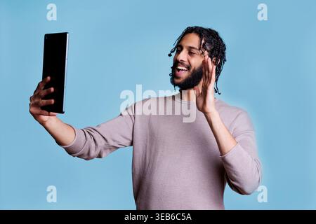 Smiling arab man waving hi during video call on digital tablet using online meeting software app. Cheerful person greeting friend while having virtual communcation in videoconference Stock Photo