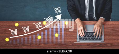 Professional businessman using a laptop to analyze e-commerce growth trends with shopping carts and financial graphs on a wooden desk, symbolizing Stock Photo