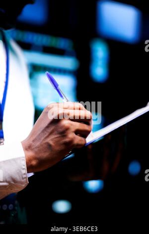Close up shot of diligent engineer equipped with maintenance checklist in data center. Admin carefully examining critical systems in high tech establishment searching for irregularities Stock Photo