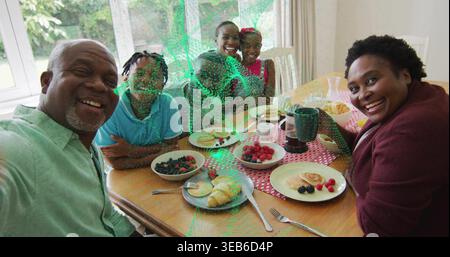 Taking selfie senior man holding smartphone while family leaning in at home dining table, pancakes Stock Photo