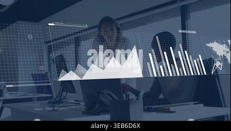 Working two women reviewing data at desk in office, wearing professional attire with data overlay Stock Photo