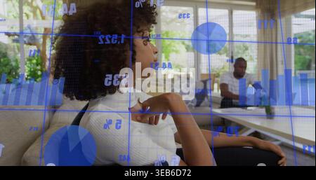 Leaning woman in white top on sofa at home, man at table using laptop, data overlay Stock Photo