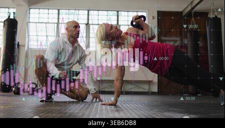 Holding plank woman in pink top doing kettlebell row in gym coach kneeling watching data overlay Stock Photo