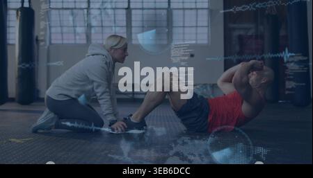 Kneeling woman in gray hoodie holding trainee's feet, man in red-top doing sit-ups in gym, overlays Stock Photo