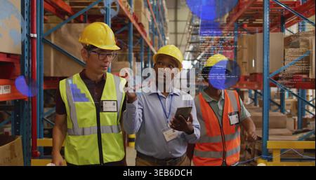 Walking team doing inventory in warehouse, wearing hardhats and vests holding tablet and showing AR Stock Photo