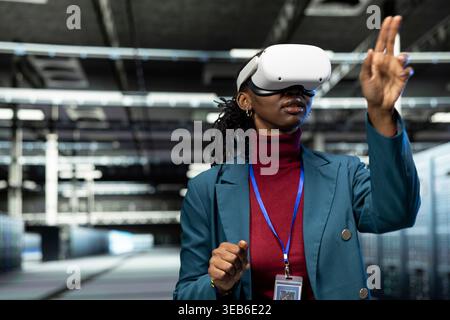Configuring server settings, VR headset gear and female programmer in data center. Using virtual reality technology, IT infrastructure and specialist in high tech server hub doing maintenance tasks Stock Photo