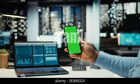 Black male consultant in office uses green screen on smartphone after hours, scheduling new meetings and planning the weekly agenda. Business management tasks for a company project. Stock Photo